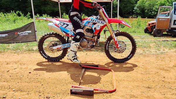 Motocross rider sitting on a dirt bike about to engage the foot petal to reset their Holeshot Pro race gate their practicing with.